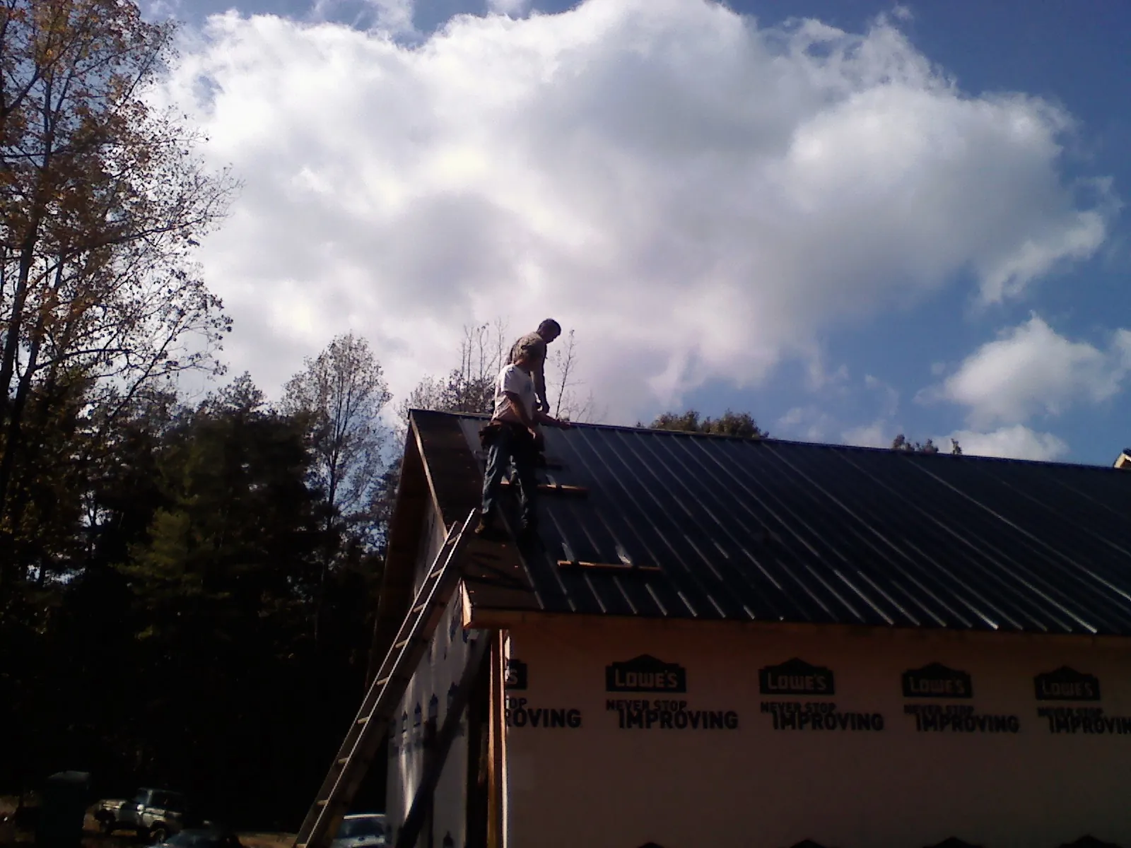Roofer fastening dark metal panels high against a cloudy sky, from a Roof Inspection job in Jeffersonville