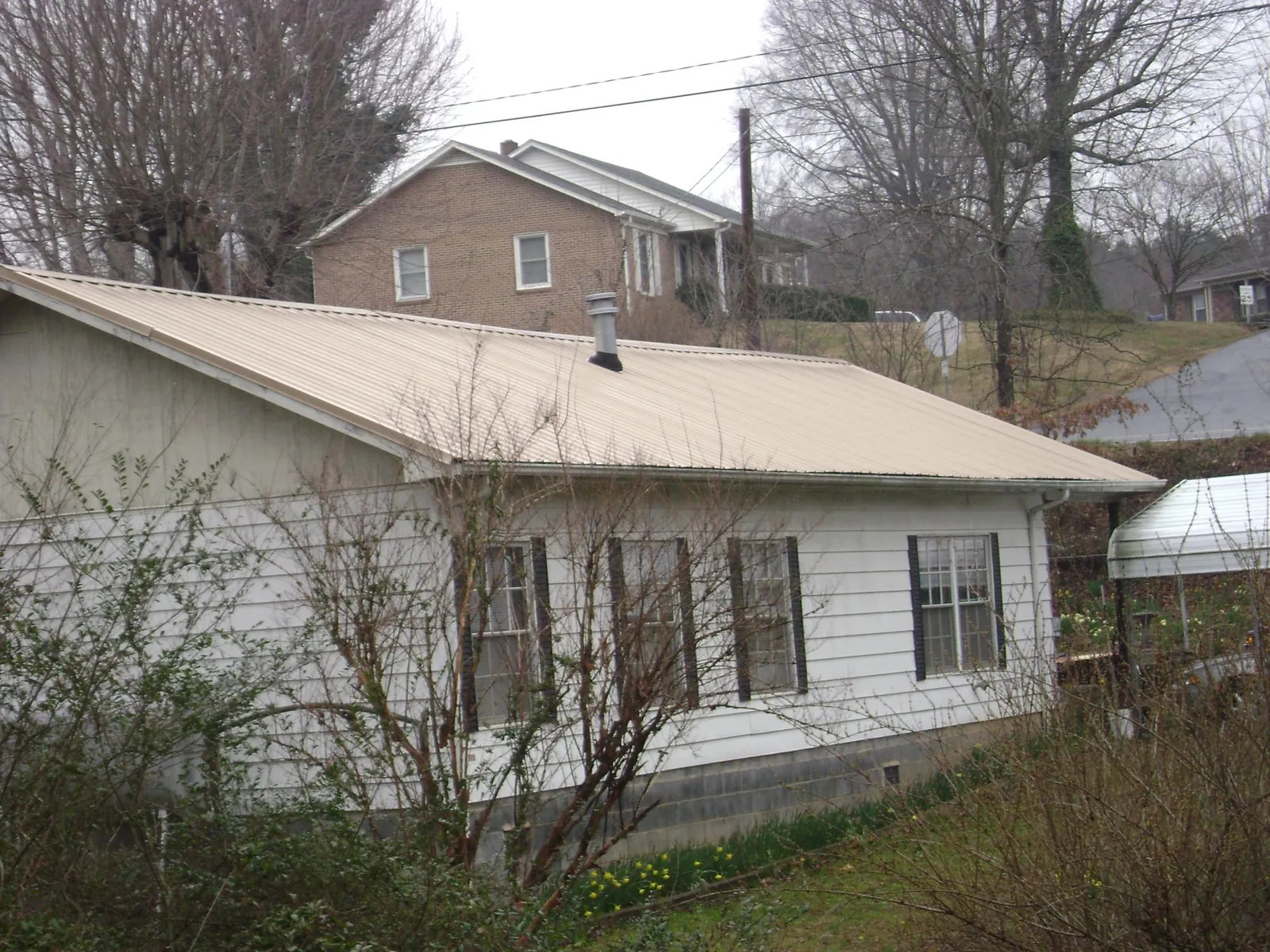 Tan metal roof on a white sided house set into a hillside — Commercial Roofing by Roofing Brothers in Jeffersonville